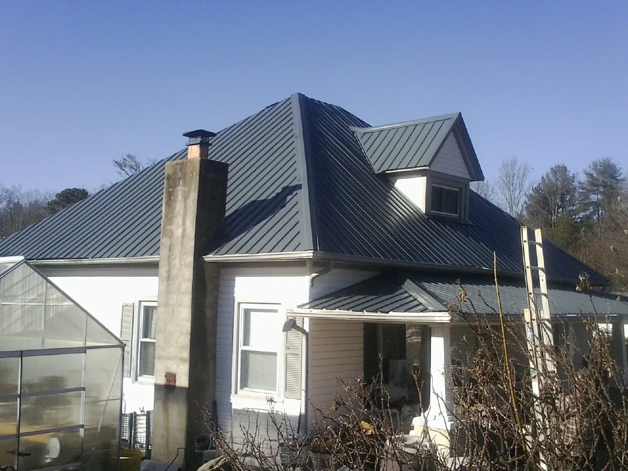 Dark blue standing seam metal roof on a white farmhouse with dormer — Slate & Tile Roof Repair by Roofing Brothers in Carrier