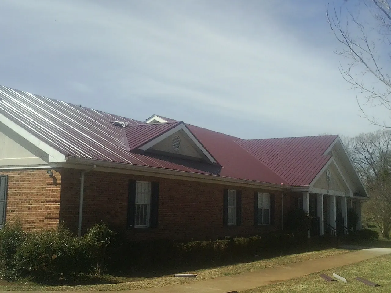 Red metal roof with gabled entries on a long brick building, from a Hail Damage Roof Repair job in Carrier