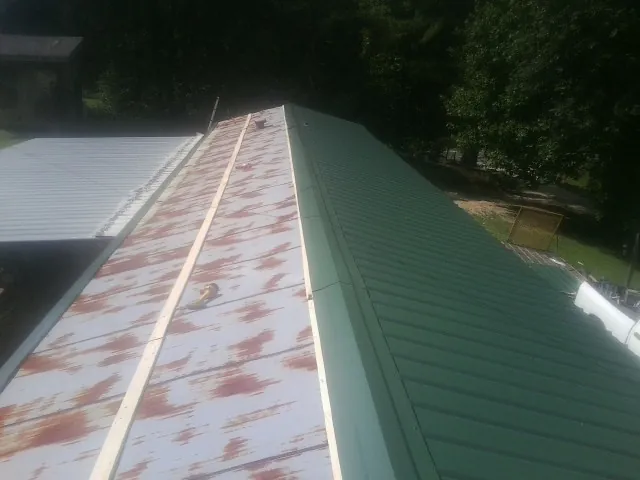 Old rusted panels beside newly installed green metal roofing — Wind Damage Roof Repair by Roofing Brothers in Carrier