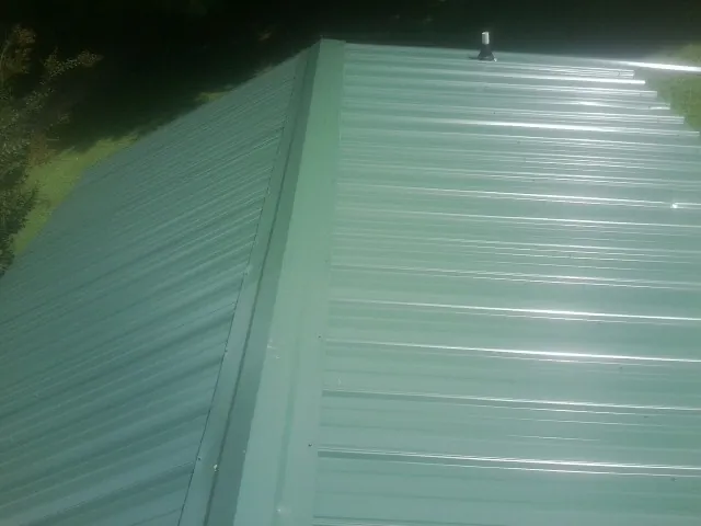 New green metal panels meeting at the ridge of a roof — Flat Roof Repair work by our crew in Carrier
