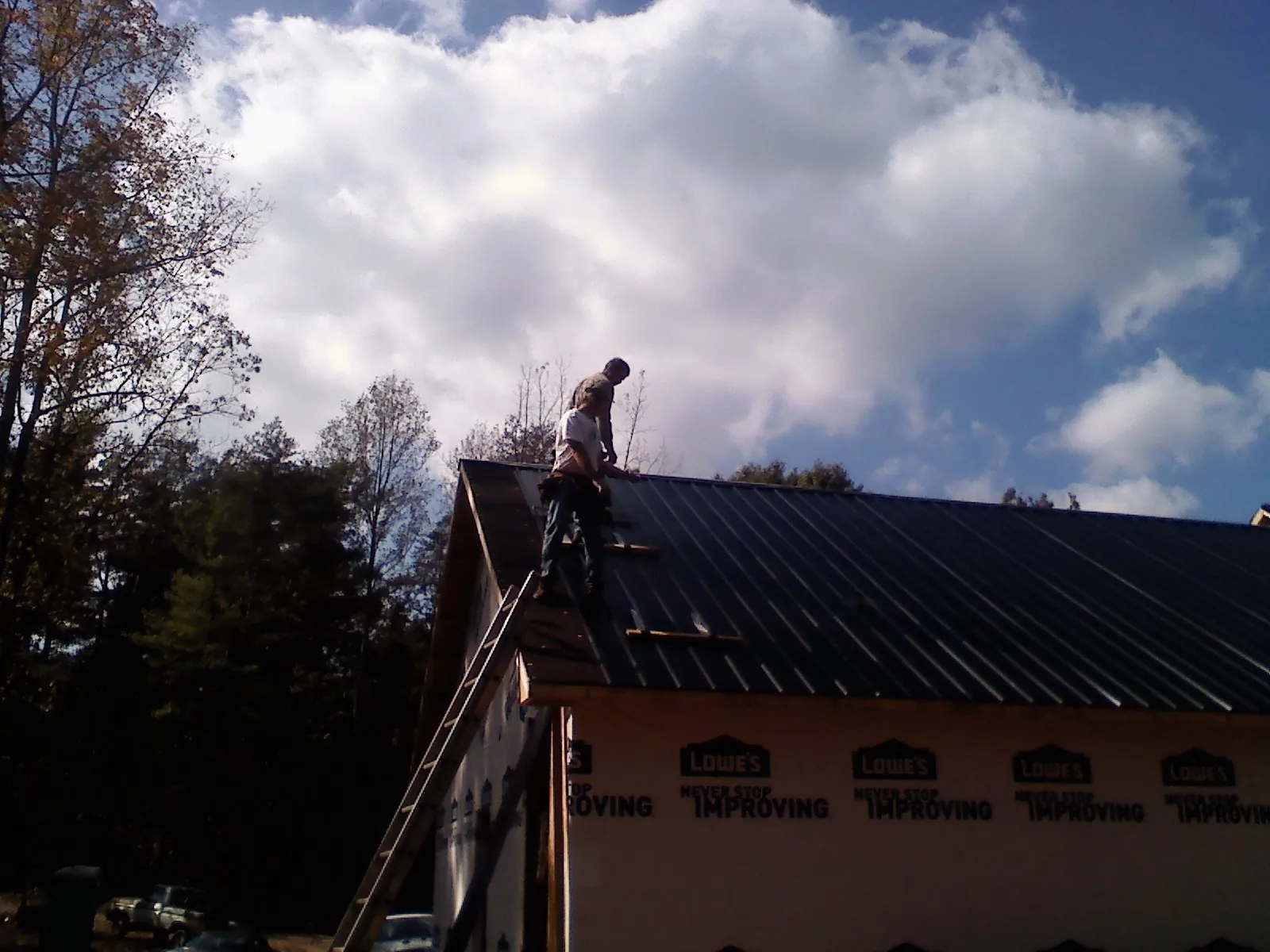 Roofer fastening dark metal panels high against a cloudy sky, from a Roof Inspection job in Carrier