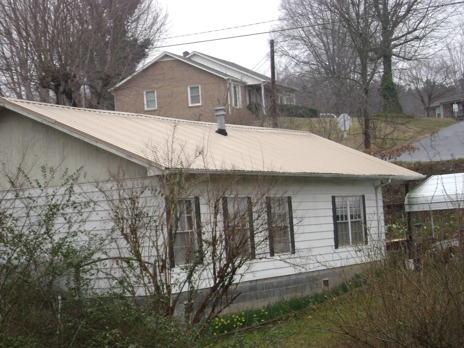 Tan metal roof on a white sided house set into a hillside — Commercial Roofing by Roofing Brothers in Carrier