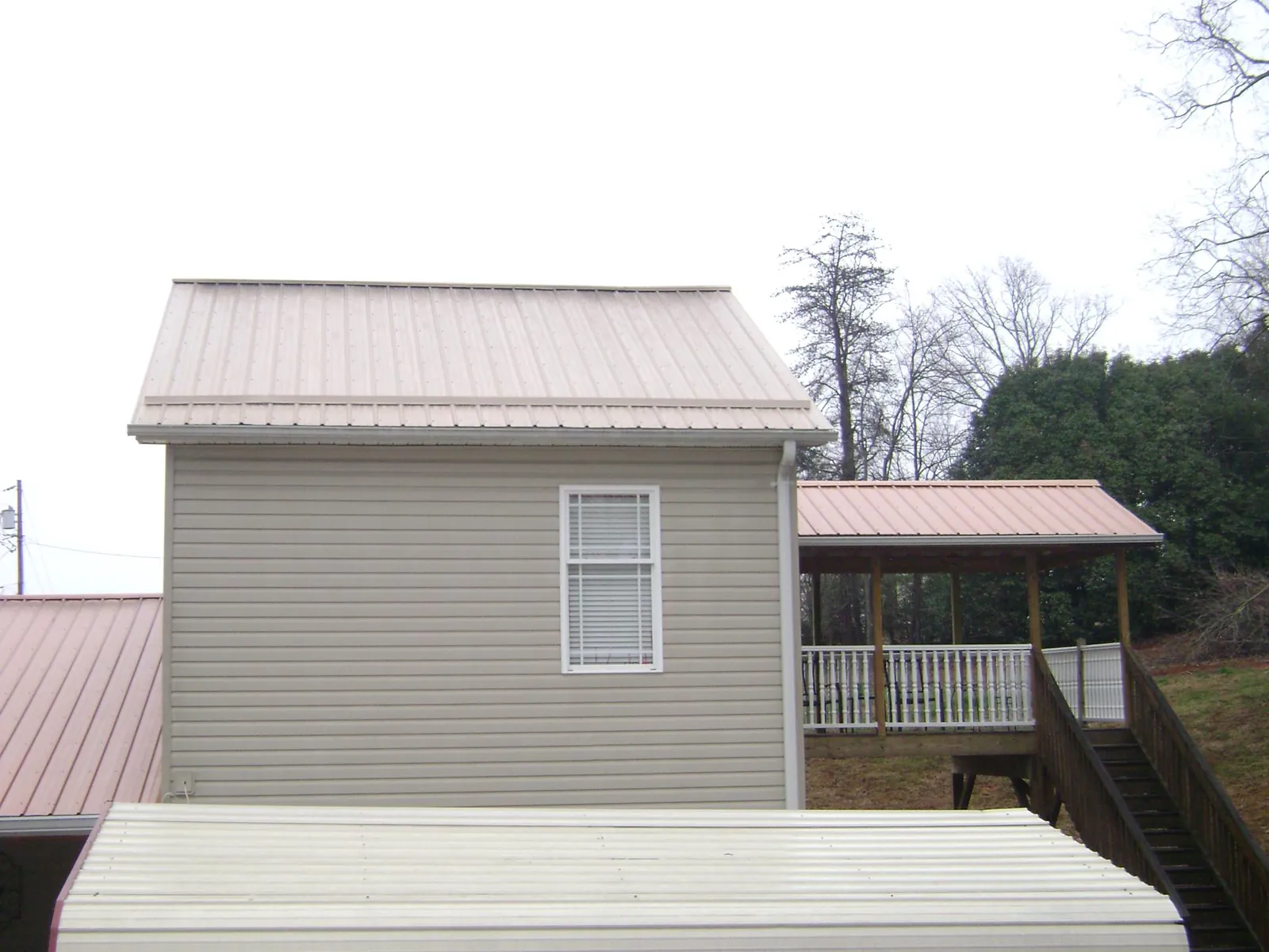 Tan metal roofs on a two story addition and attached porch, from a Roof Replacement job in Carrier