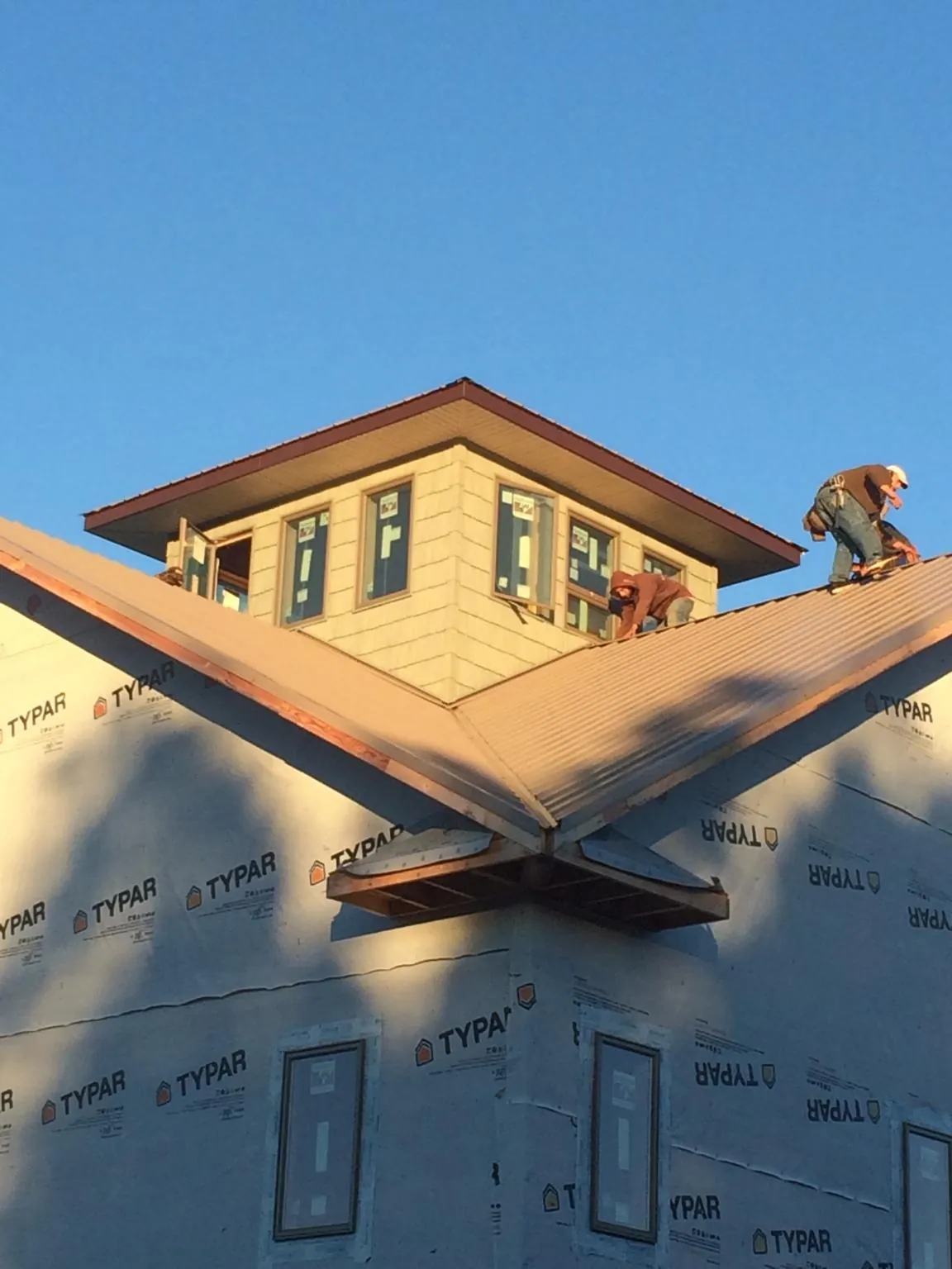 Roofers working around a rooftop cupola on a new metal roof at sunset — Roof Waterproofing in Carrier by Roofing Brothers